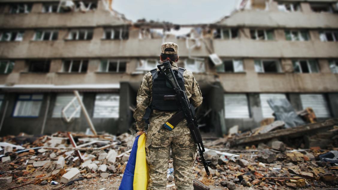 Ukrainian soldier holding a national flag, standing before a bombed-out apartment building